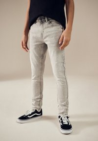 Jean skinny gris délavé avec braguette zippée et fermeture par bouton, comportant une couture latérale noire, associé à des baskets Vans noires.