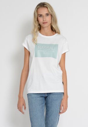 White cotton t-shirt with rolled sleeves, featuring a light blue rectangular logo that says "NASSAU BEACH CLUB Ibiza." Paired with blue jeans.
