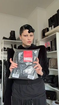 Fekete ruházat tiszta műanyag tasakban csomagolva, piros "DIESEL" címkével, a háttérben színes grafikákkal ellátott polcon.