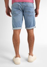 Shorts di denim azzurro chiaro con risvolti, dotati di due tasche posteriori. Abbinati a sneakers color crema. Pelo delle gambe e texture della pelle visibili.