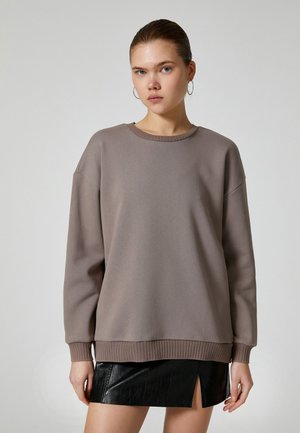 Grå oversized sweatshirt med rund halsringning och ribbad fåll, kombinerad med en svart faux läderkjol med en sidoflik.