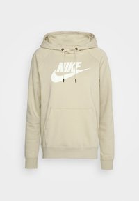 Béžová mikina s kapucí, kapsou kangaroo, stahovací šňůrkou a bílým logem Nike na hrudi. Vyrobená z měkké, strukturované látky.