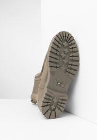 Beige suede ankle boot with a ridged rubber sole, featuring a textured upper and logo detail on the insole. Tapered silhouette with a slight heel.