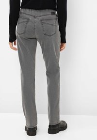 Pantaloni in denim grigio con taglio dritto, dotati di doppie tasche posteriori e una finitura leggermente testurizzata. Indossati con stivali neri alla caviglia.