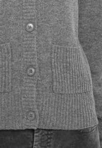 Šedý cardigan s ribbovanou texturou, se šesti knoflíky a dvěma předními kapsami. Měkká tkanina s prostředním pletením.