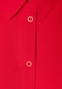 Rode poloshirt met een puntige kraag, textuur stof en twee bijpassende knopen langs de knoopsluiting. Close-upweergave benadrukt de details.