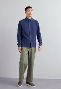 Navy button-up shirt with ribbed texture, long sleeves, and a rounded collar, paired with olive green wide-leg trousers and gray sneakers.