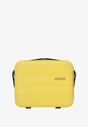 Étui rigide jaune avec une surface texturée, fermeture éclair et sangle noire ajustable. Présente un logo American Tourister à l'avant.