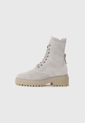 Bottines en suede gris clair avec bout rond, lacets à l'avant et semelle chunky beige. Présente des œillets dorés et une languette à l'arrière.