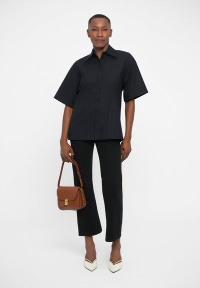 Camisa de manga corta a rayas negras, pantalones acampanados negros, tacones blancos de punta y un bolso cruzado marrón con un cierre dorado.