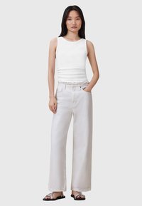 Top de tirantes blanco ajustado con escote redondeado, combinado con pantalones vaqueros blancos de corte holgado. La modelo lleva chanclas negras.