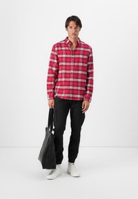 Camisa de cuadros roja y blanca de botones, pantalones cargo negros, zapatos blancos y una bolsa tote negra. Diseño simple con un ajuste relajado.