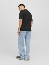 Schwarzes Baumwoll-T-Shirt, leicht tailliert, mit kurzen Ärmeln. Tragen mit hellblauen, locker sitzenden Jeans und grauen Sneakers.
