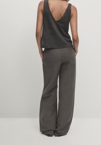 Top a righe nera con scollatura a V profonda sul retro, abbinata a pantaloni in lino grigi chiari, morbidi e con tasche posteriori, caratterizzati da una silhouette rilassata.