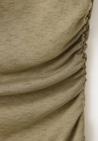 Tissu beige texturé avec des plis froncés et des bords froncés créant des plis superposés sur un fond clair.