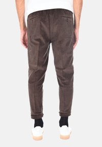 Pantaloni di velluto a coste marroni con righe verticali, dotati di tasche posteriori e una vestibilità affusolata, abbinati a sneakers bianche e calzini neri.