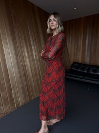 Κόκκινο διάφανο φόρεμα με μαύρα μοτίβα φύλλων και λεοπάρ, μακριά μανίκια και ρέουσα σιλουέτα, συνδυασμένο με nude σανδάλια.