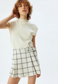 Lichtbeige gebreide top met korte mouwen, gecombineerd met een witte geruite minirok met een zijgesp en een textuurstof.