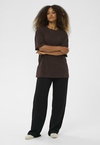 T-shirt marrone oversize con scollo rotondo abbinato a pantaloni a gamba larga neri. Texture visibile nel tessuto; la vestibilità rilassata migliora il comfort.