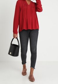 Rood gestippeld blouse met lange mouwen en een V-hals, gecombineerd met zwarte skinny jeans en bruine instappers. Inclusief zwarte handtas met textuur.