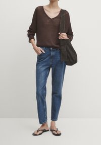 Pull en tricot marron avec un col en V, jean en denim bleu et tongs noires. Équipé d'un sac à bandoulière en suède noir. Design simple et décontracté.