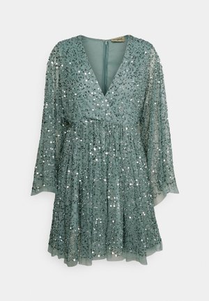 Mini abito verde a maniche lunghe con scollo profondo a V e paillettes argentate su tessuto trasparente, gonna svasata e chiusura con zip sul retro.