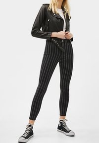 Černá kožená motorkářská bunda se stříbrnými zipy, doplněná černo-bílými pruhovanými úzkými džíny. Outfit doplňují černé kotníkové tenisky.