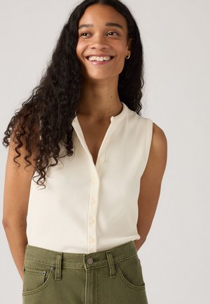 Haut sans manches en crème à côtes avec un col rond et une fermeture à boutons à l'avant. Associé à un pantalon taille haute vert olive.