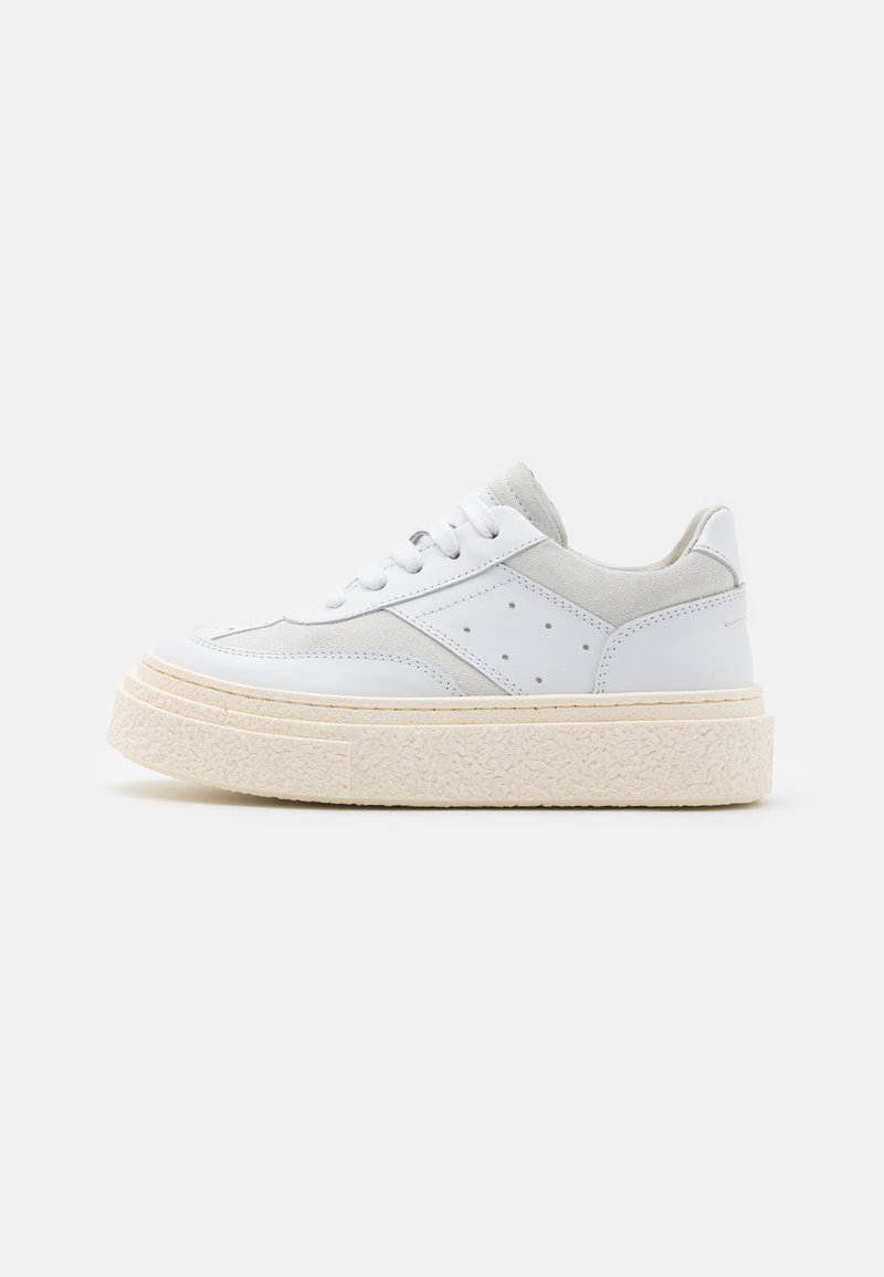 Hvit lær sneaker med grå semsket skinnaksenter, flate hvite snøringer, teksturert, tykk såle og perforerte detaljer på sidene.