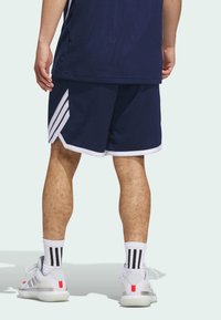 Shorts deportivos de color marino con ribete blanco, tres rayas blancas a los lados, combinados con calcetines blancos con rayas negras y zapatillas grises.