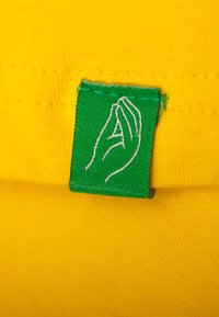 Groen geweven label met een handenafbeelding, genaaid op een felgele stof, met een gladde textuur en gelijkmatige stiksels.