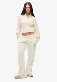 Crèmekleurige cropped kabelbrei trui en bijpassende brede sweatpants met een trekkoord in de taille en een gedrukt logo op de linkerdij.