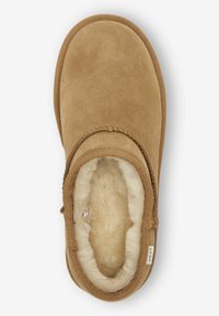 Tan farvet ruskinds slip-on sko med en blød, beige fleeceforing. Har en rund tå og kvast detaljering langs åbningen. Flad sål.