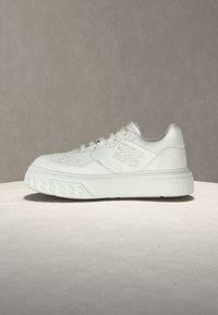 Λευκό αθλητικό παπούτσι με λείο δερμάτινο επάνω μέρος, στρογγυλεμένη μύτη, κορδόνια στο μπροστινό μέρος και υφή στην σόλα με σχέδιο αλυσίδας στις πλευρές.