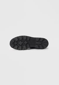 Black rubber shoe sole with deep treads and a patterned surface. Features grooves and circular accents for traction and grip.