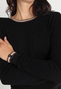 Czarny dziany sweter z okrągłym dekoltem, z teksturowanym, wielokolorowym paskiem przy mankietach. Miękki materiał o dopasowanym kroju.