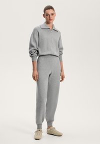 Gray knit tracksuit with a collared zip-up top and elastic waistband pants. Soft texture, relaxed fit, and ribbed cuffs. Casual sneakers.