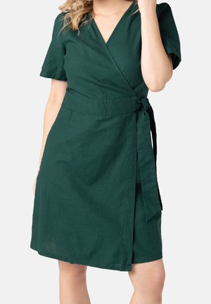 Robe portefeuille verte avec un décolleté en V, des manches courtes et un détail de ceinture nouée à la taille. Confectionnée dans un tissu texturé et respirant.