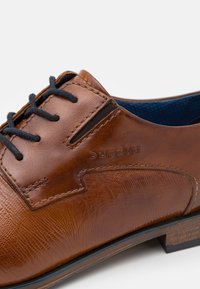 Chaussure habillée en cuir marron avec une surface texturée, des lacets noirs et un intérieur bleu foncé. Présente un design minimaliste et un détail de logo subtil.