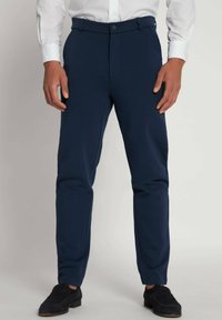 Marineblå bukser lavet af strækbart stof, med en slim fit, bæltesløjfer og lukning med frontknap, parret med sorte sko.