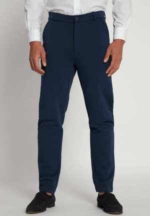 Navy blue trousers made of stretchy fabric, featuring a slim fit, belt loops, and a front button closure, paired with black shoes.