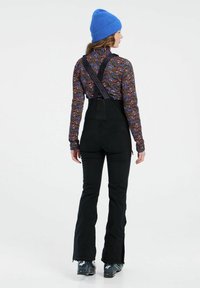 Čierny overal s nastaviteľnými popruhmi, skombinovaný s dlhým rukávom košeľou s mnohými farbami a modrou pletenou čiapkou. Slim-fit nohavice s rozšírenými nohami.