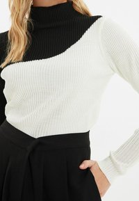 Jersey de cuello vuelto acanalado con diseño en bloques de color negro y blanco, mangas largas y forma ajustada. Tejido de punto texturizado.