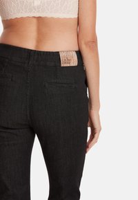 Zwarte denim broek met een getextureerde tailleband label. De achterkant heeft twee zakken en een slim fit ontwerp, met een gladde stofoppervlak.