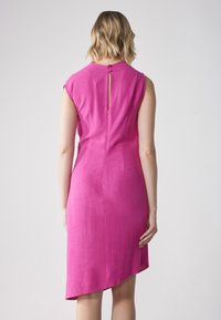 Robe fuchsia à manches courtes, avec un détail en forme de clef au dos et un ourlet asymétrique, fabriquée à partir d'un tissu texturé.