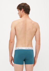 Egy pár türkiz boxer alsónemű, puha anyagból készült, fehér derékpánttal, amelyen piros betűkkel "TOMMY HILFIGER" felirat található.