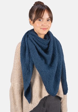 Eine marineblaue, strukturierte Wollschal liegt über einem hellbeigen Pullover und bildet eine dreieckige Form mit spitzen Enden.