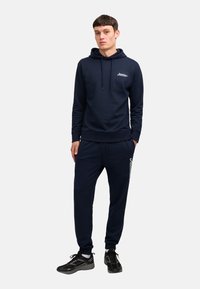 Navy bluza z kapturem i dresy w miękkim materiale, wyposażone w tasiemkę przy kapturze, elastyczne mankiety oraz logo na nogawce.