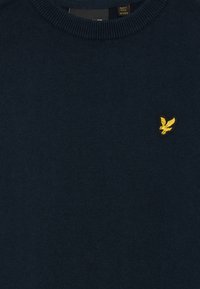 Tamsiai mėlynas megztinis su nėriniais, su apvalia iškirpte ir maža geltona išsiuvinėta paukščio logotipu kairiajame krūtinės kampe.