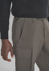 Pantaloni cargo grigi con davanti piatto, tasche laterali e tessuto testurizzato. La vita presenta un dettaglio di chiusura discreto.